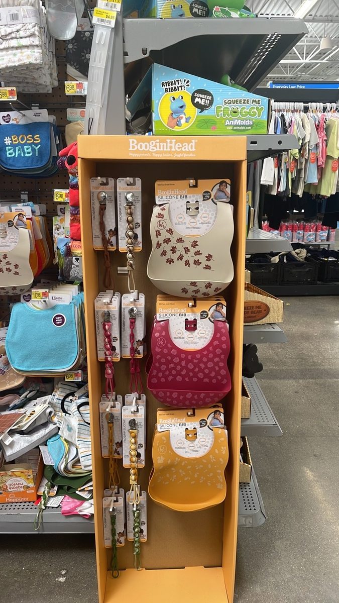 A BooginHead-branded sidekick display in the baby aisle at Walmart, stocked with silicone bibs and PaciGrip pacifier clips.